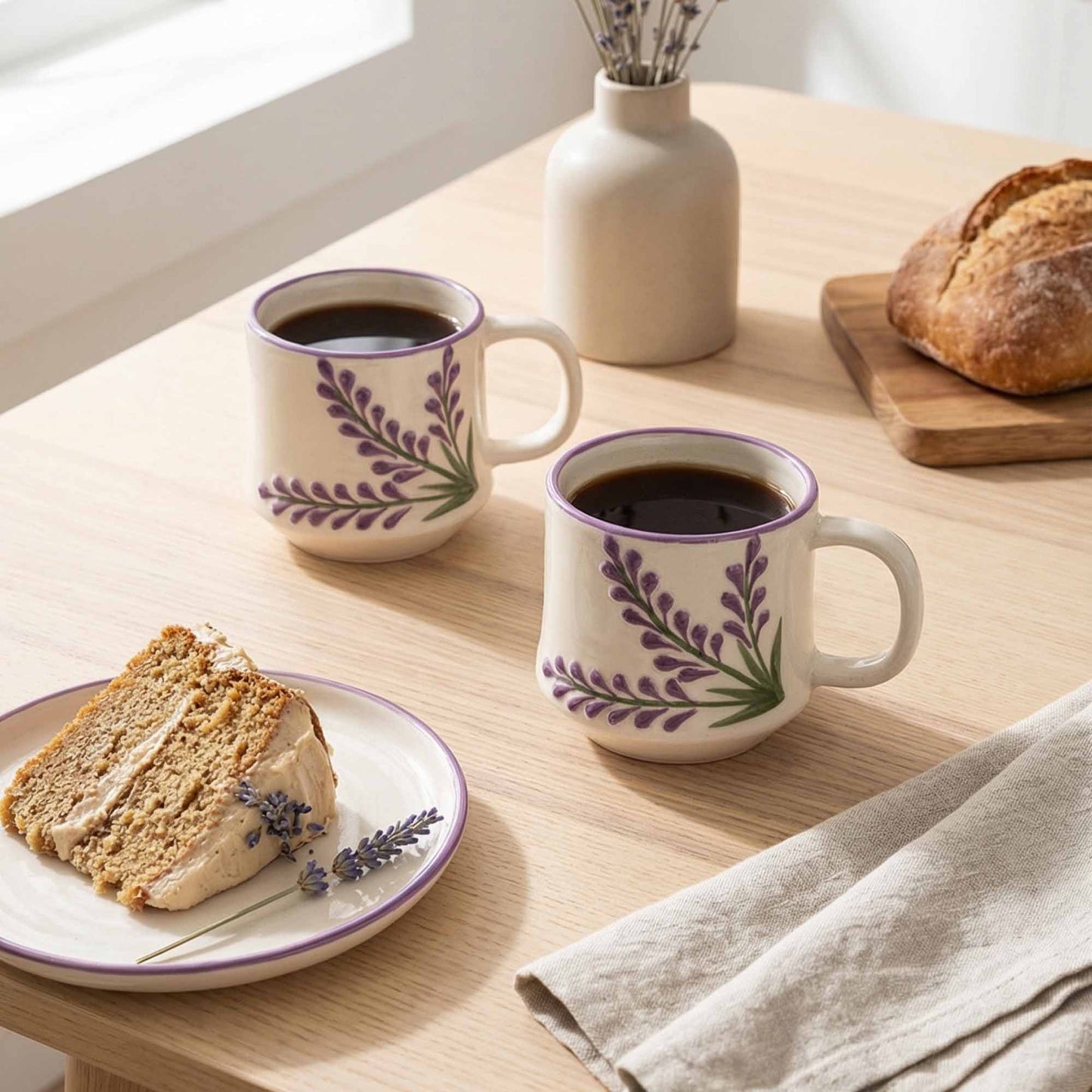 Two mugs with floral design on a wooden table with bread and cake.