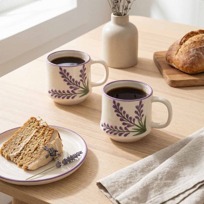 Two mugs with floral design on a wooden table with bread and cake.