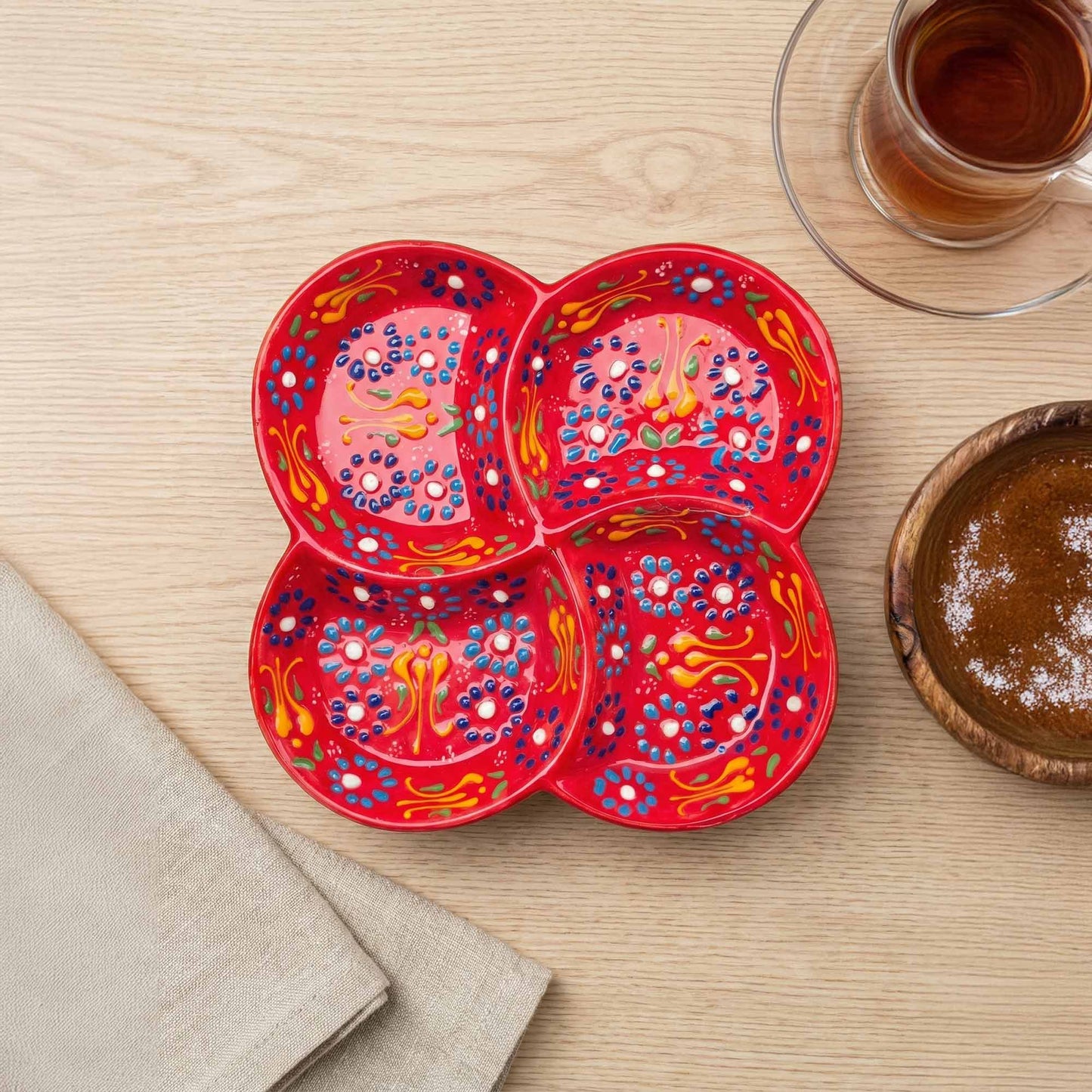 Red decorative plate with floral patterns on a wooden table with a cup of tea and a bowl.