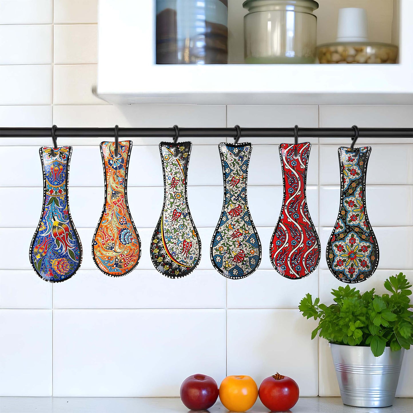 Colorful patterned spoon rests hanging on a rack against a white tiled wall with kitchen items below.