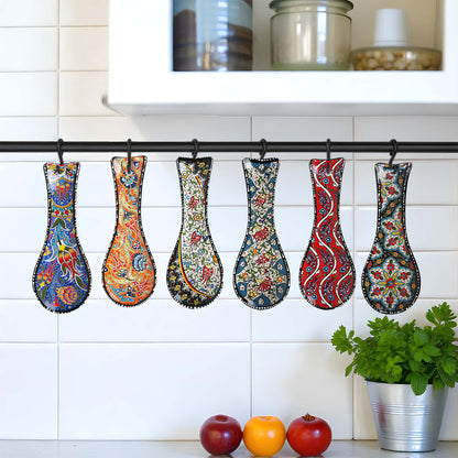 Colorful patterned spoon rests hanging on a rack against a white tiled wall with kitchen items below.
