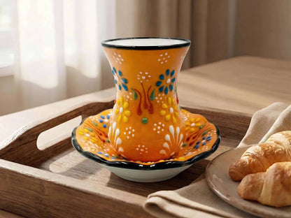 Decorative orange cup with floral patterns on a wooden tray with pastries.