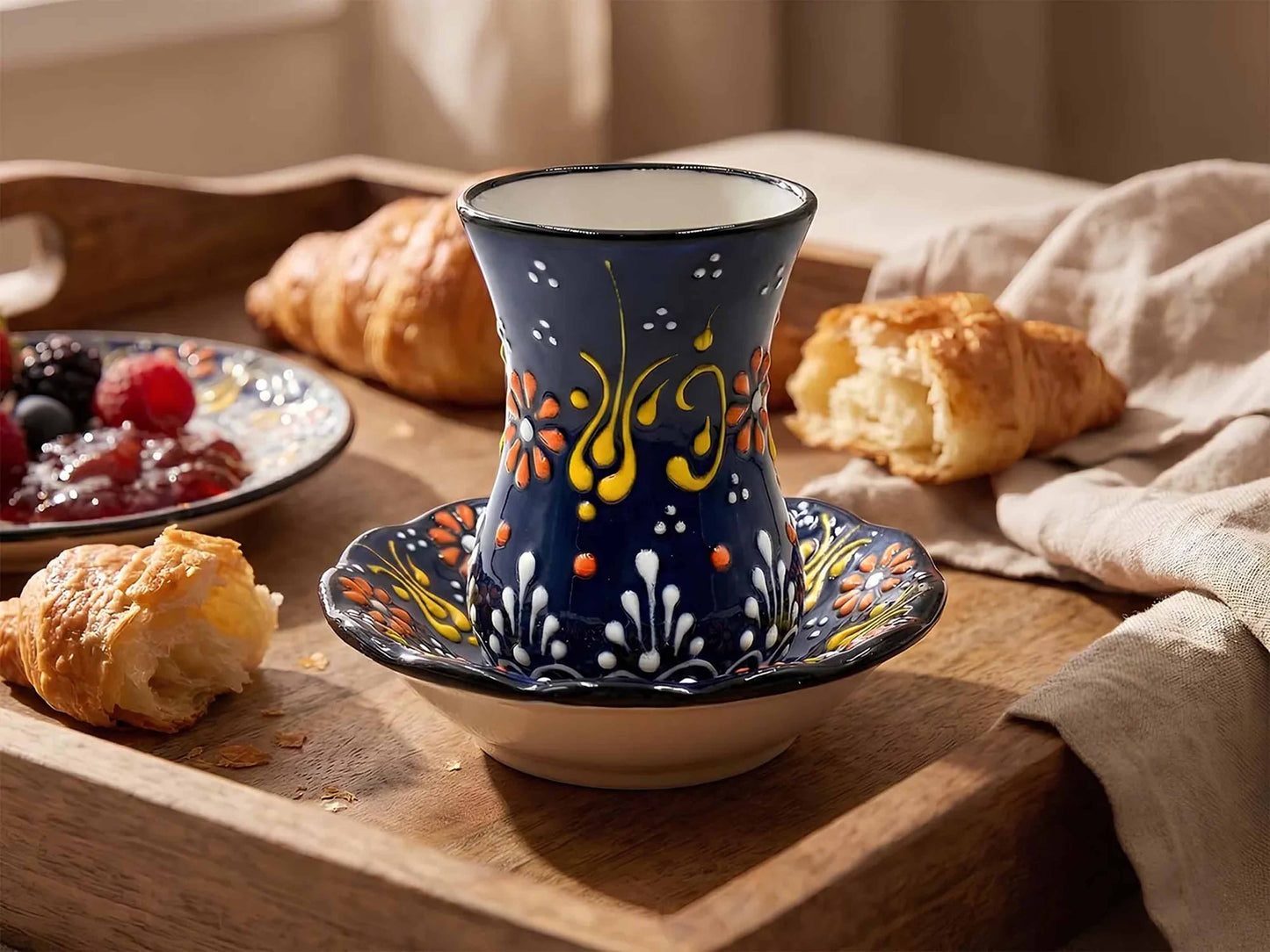 Decorative teacup with floral design on a wooden tray with pastries and jam.