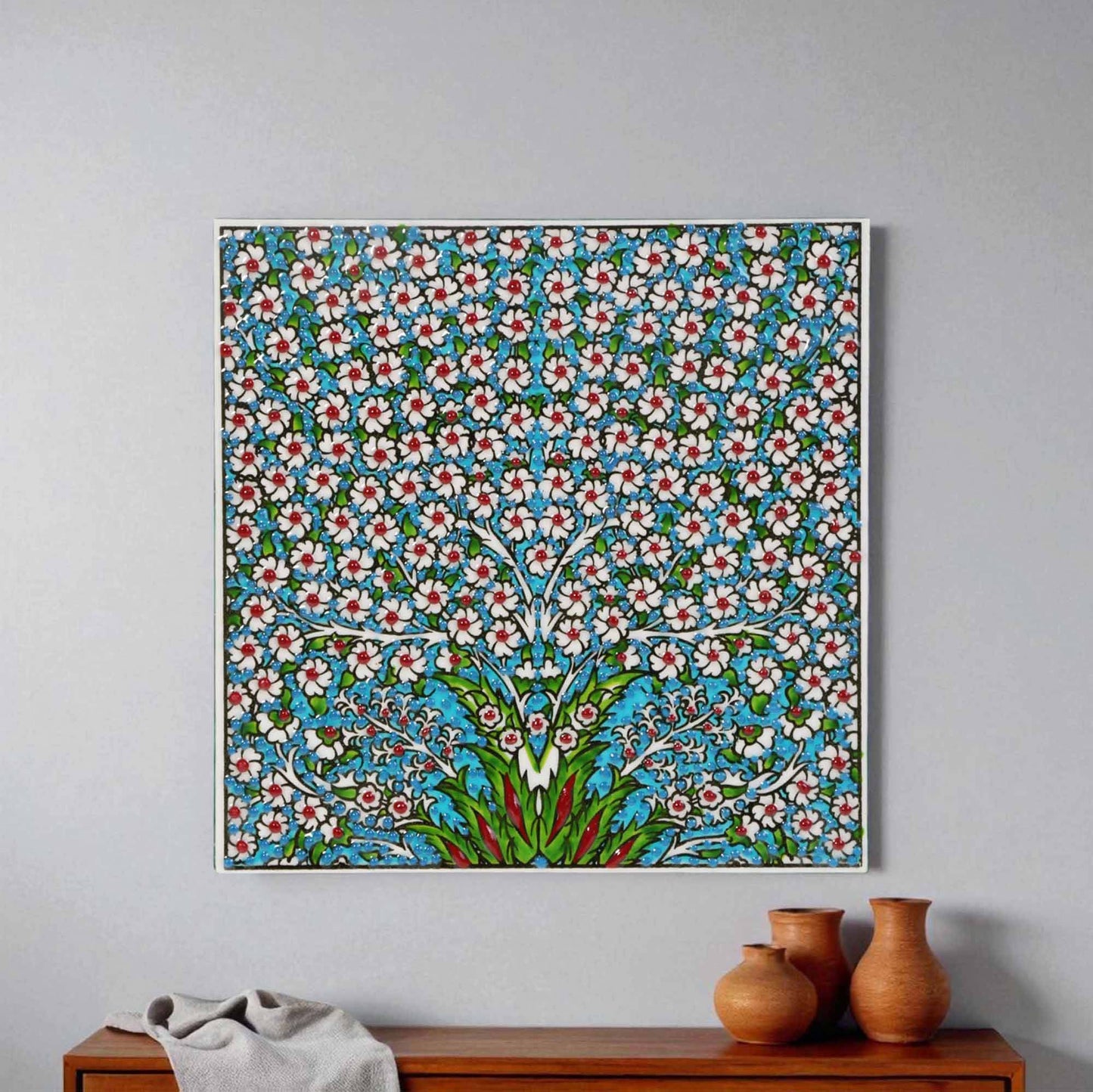 Decorative floral patterned ceramic tile wall art on a gray wall with wooden furniture and vases below.