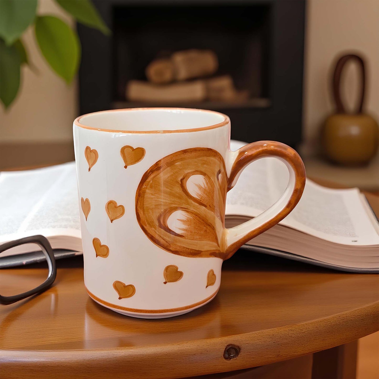 Mug with heart design on a wooden surface with a book and glasses in the background