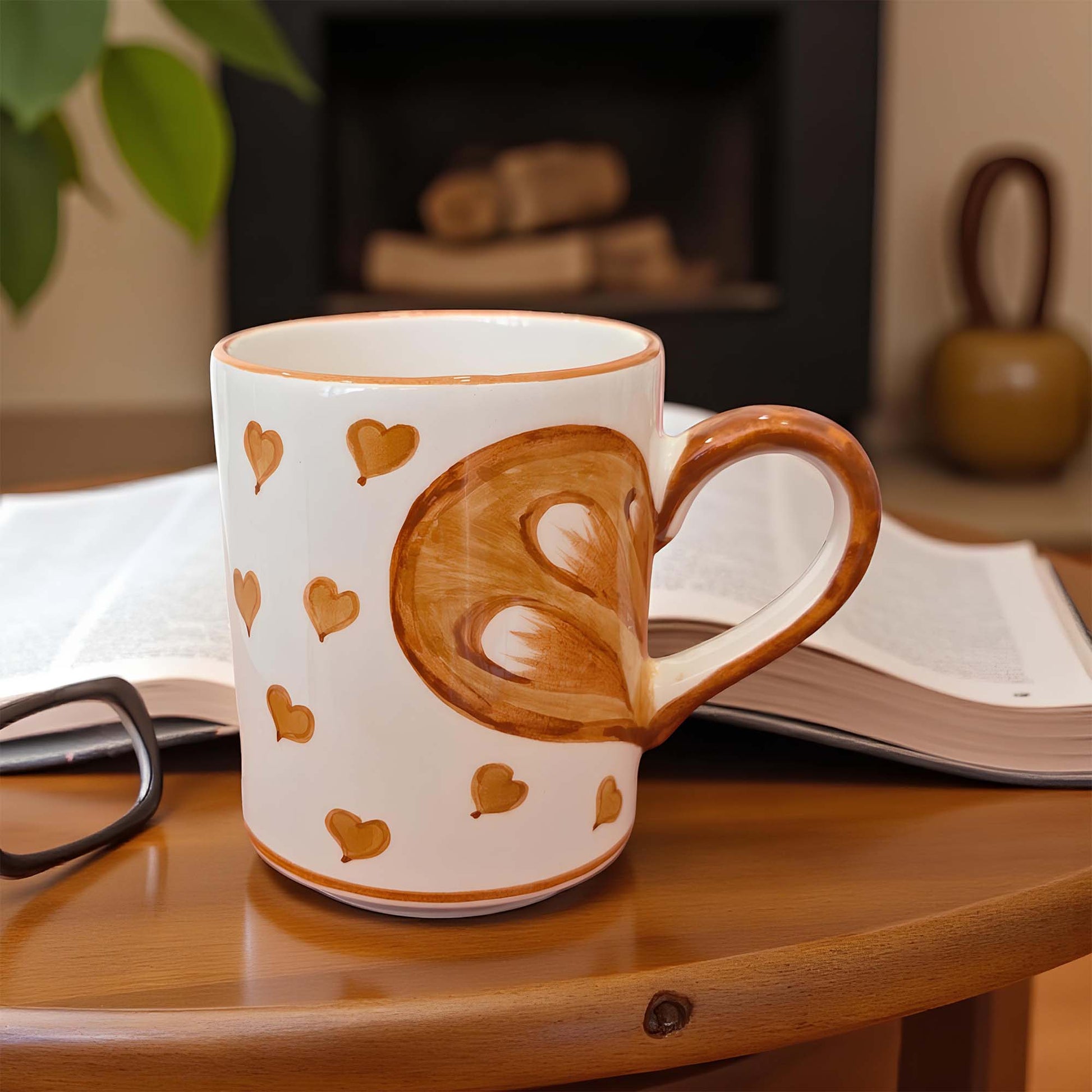 Mug with heart design on a wooden surface with a book and glasses in the background