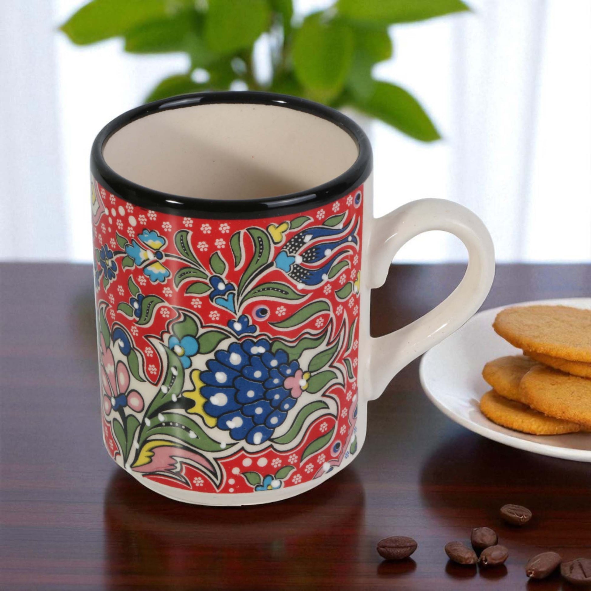 Colorful coffee mug with floral design on a wooden table with cookies and coffee beans.