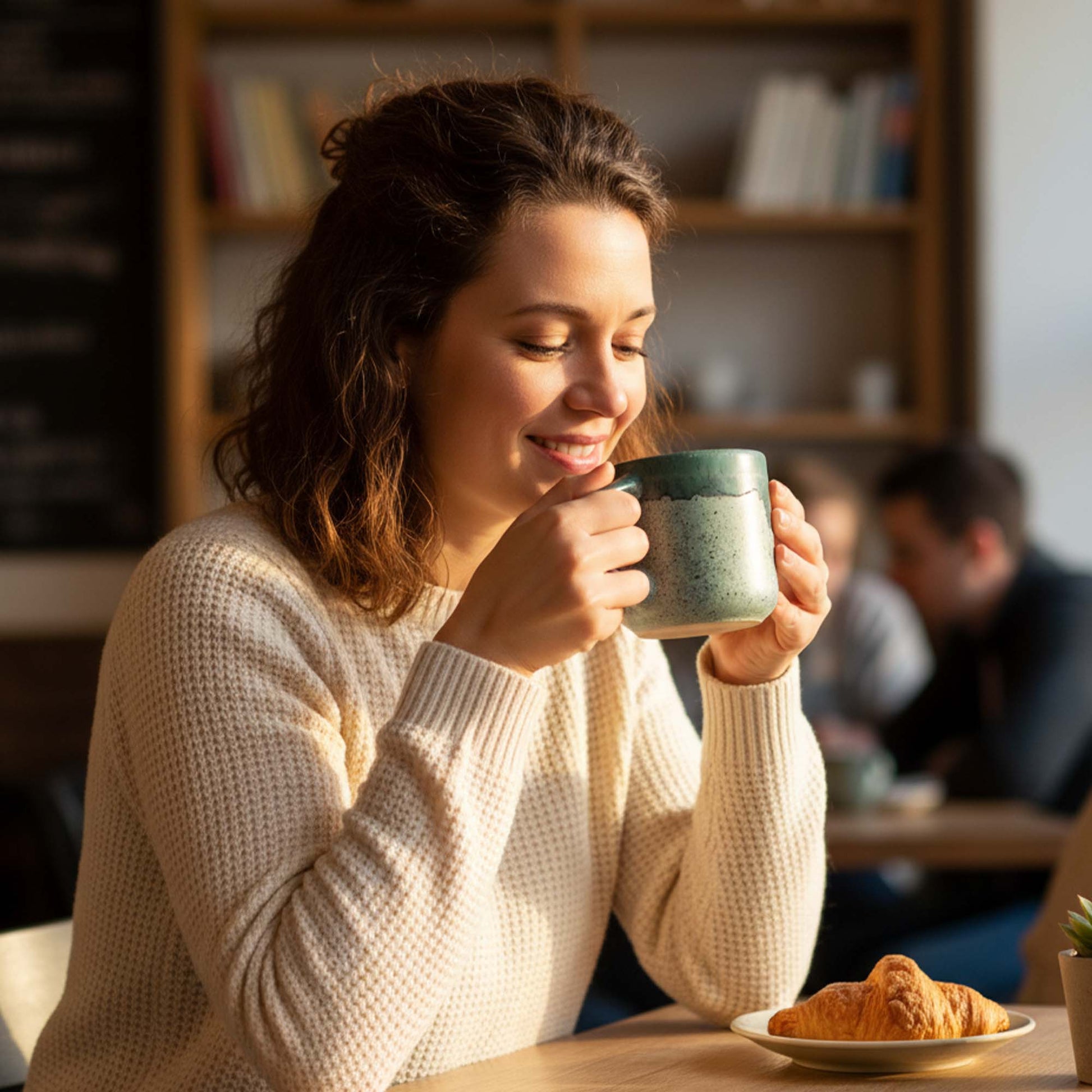 Woman enjoying a cup of coffee with a croissant at a cafe.