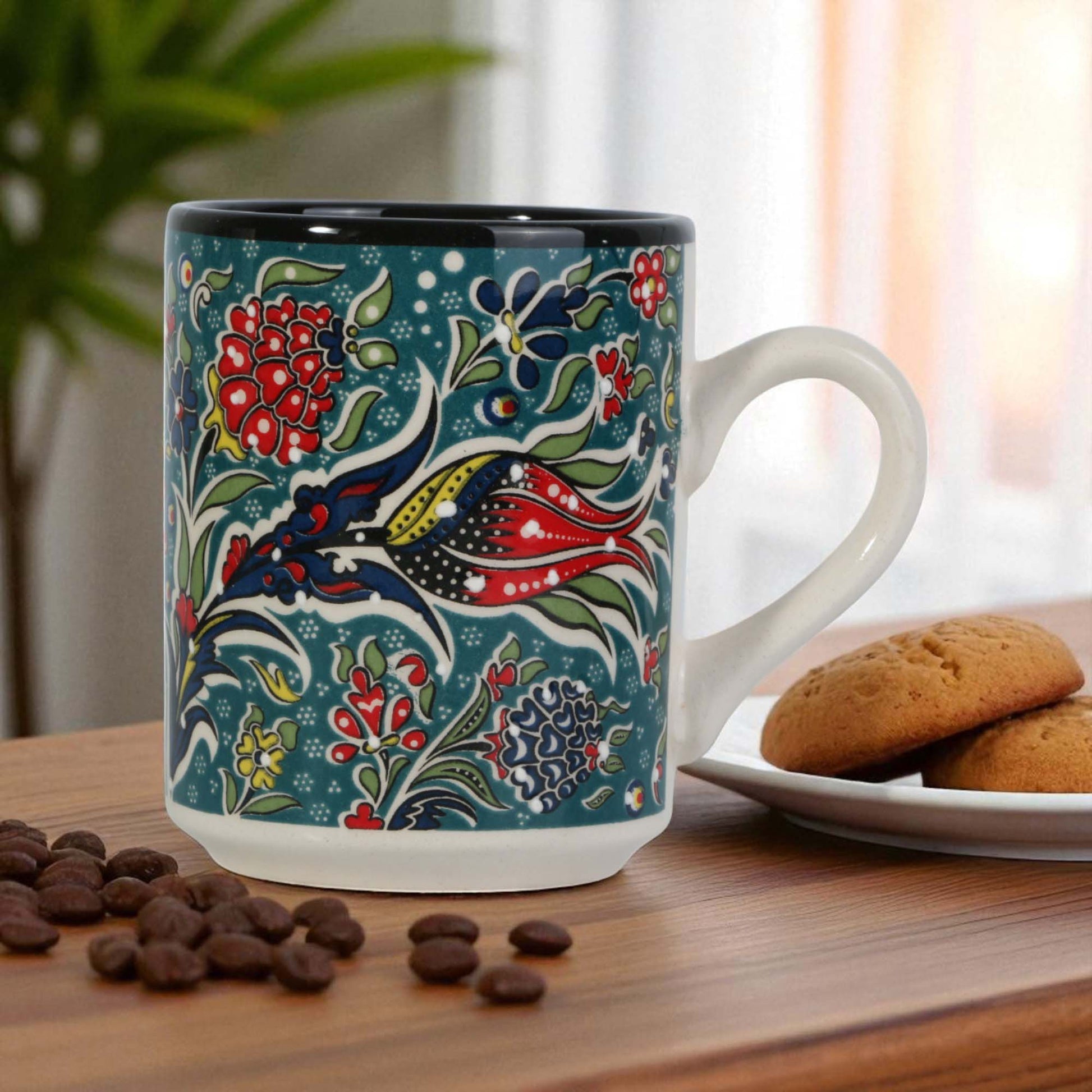 Decorative mug with floral pattern on a wooden table with cookies and coffee beans.