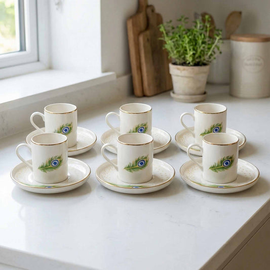 Set of porcelain cups and saucers with peacock feather design on a kitchen counter.