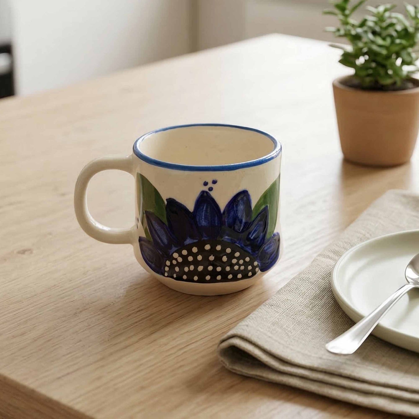 Ceramic mug with floral design on a wooden table with a plant and plates in the background