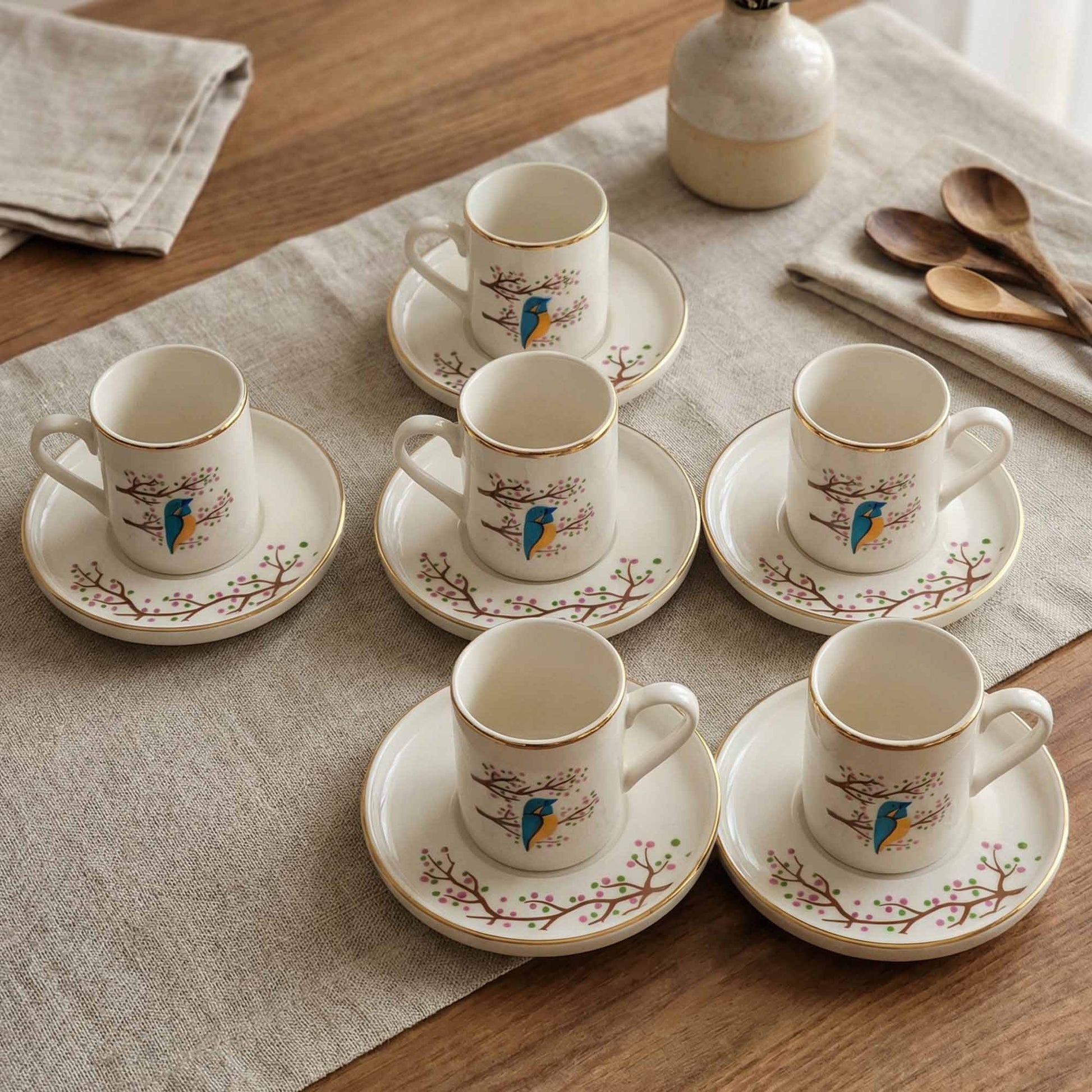 Set of porcelain cups and saucers with bird designs on a wooden table.