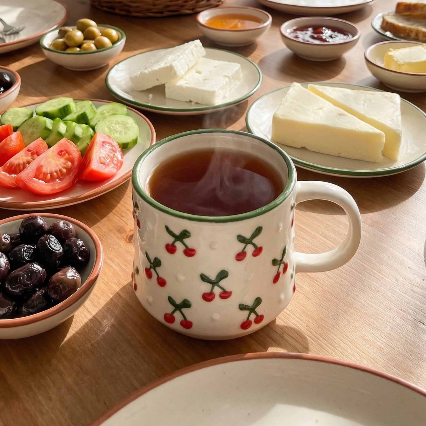 Cup of tea with a decorative pattern on a wooden table with cheese, fruits, and other snacks.