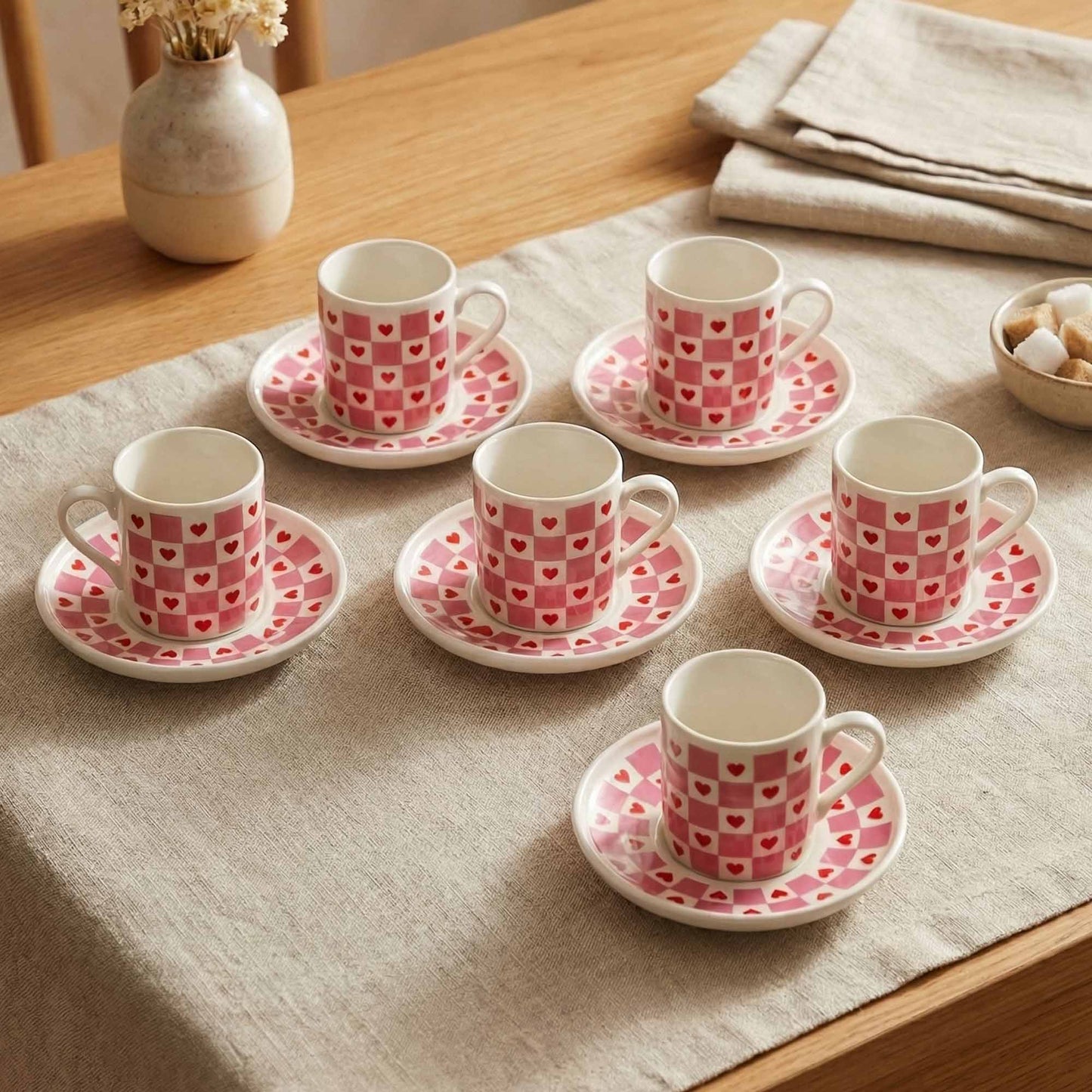 Set of six porcelain cups and saucers with heart pattern on a tablecloth.