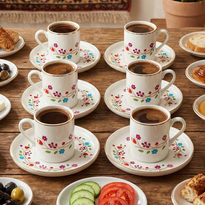 Set of floral-patterned coffee cups and saucers on a wooden table with snacks.