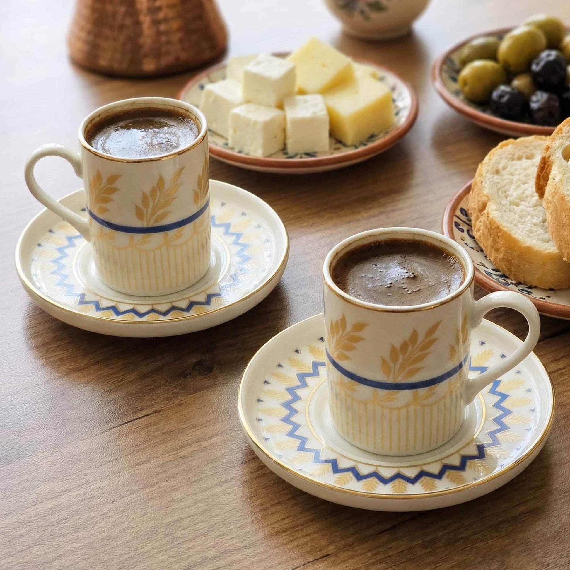 Two porcelain coffee cups with saucers on a wooden table with snacks.