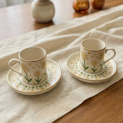 Two porcelain cups with floral designs on saucers placed on a textured fabric surface.