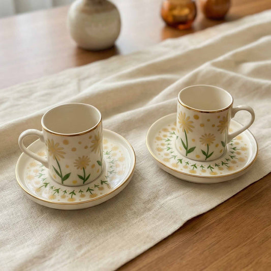 Two porcelain cups with floral designs on saucers placed on a textured fabric surface.
