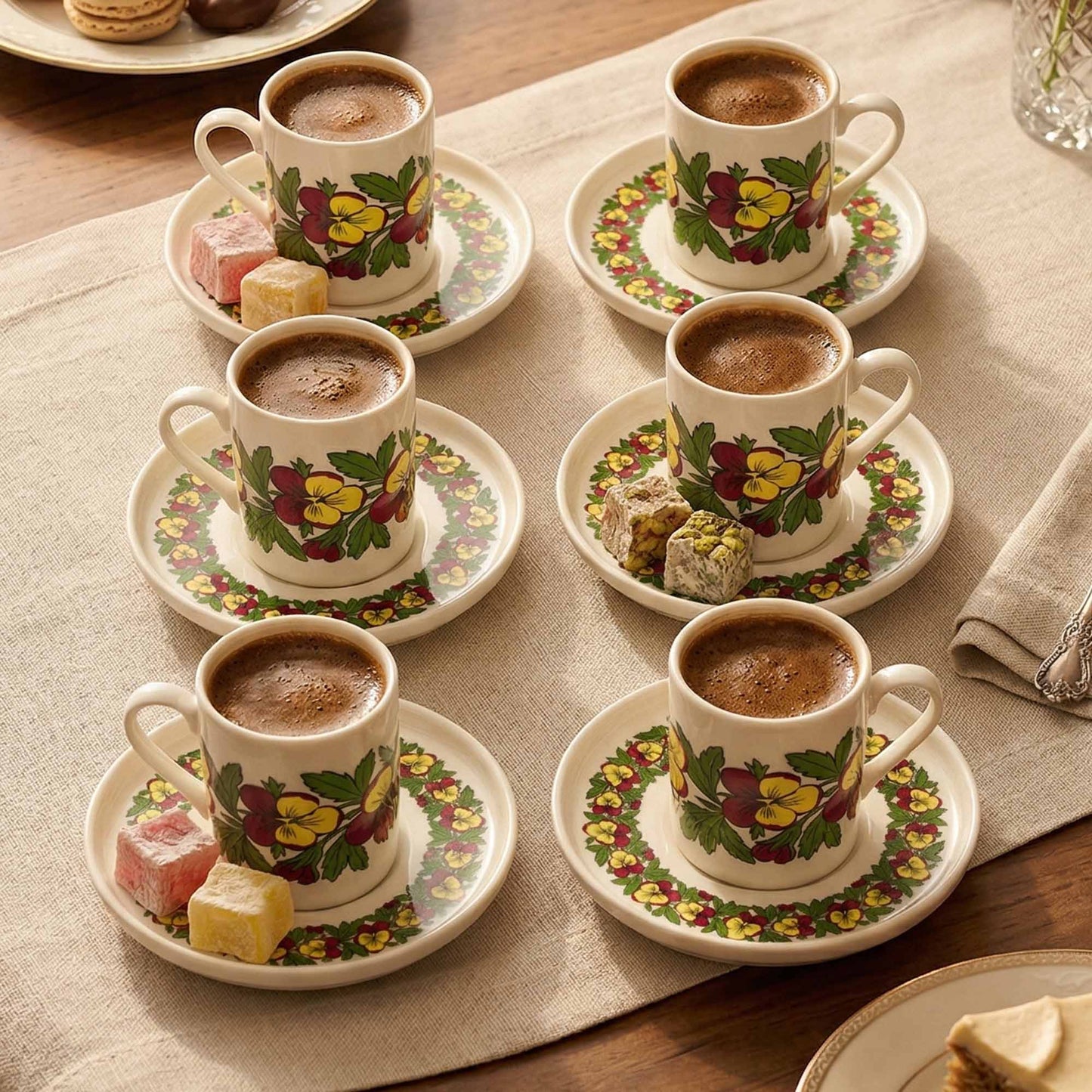 Set of six floral-patterned coffee cups and saucers with hot coffee on a tablecloth.