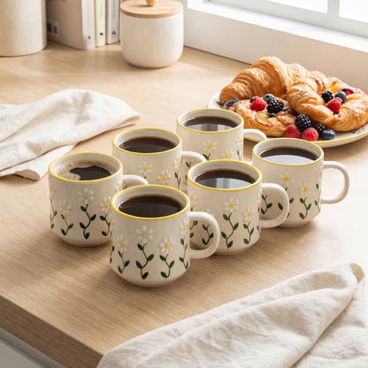 Set of ceramic mugs with floral design on a wooden table with coffee and pastries.