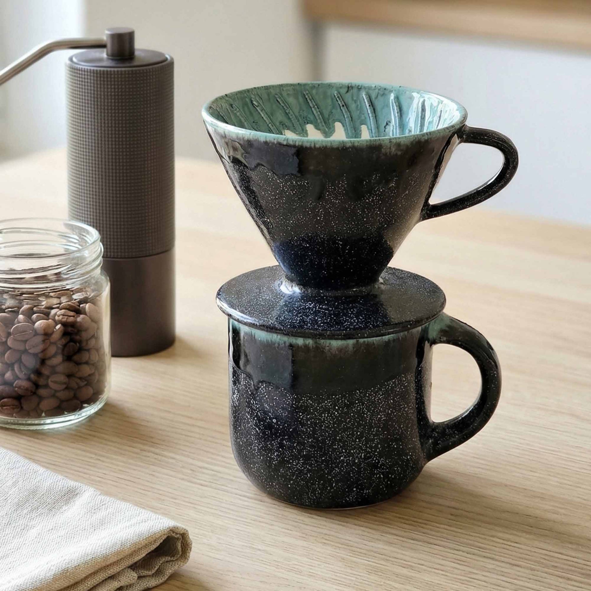 Ceramic coffee dripper with a glass container of coffee beans on a wooden surface.
