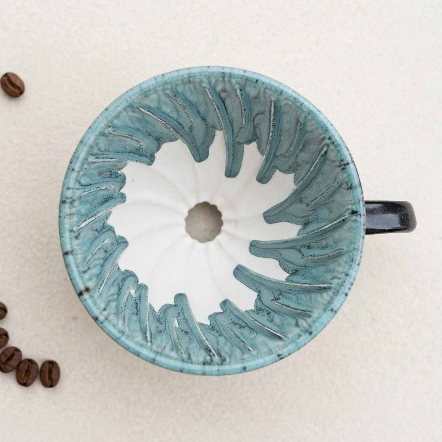 Ceramic coffee filter with textured design on a beige background with coffee beans.
