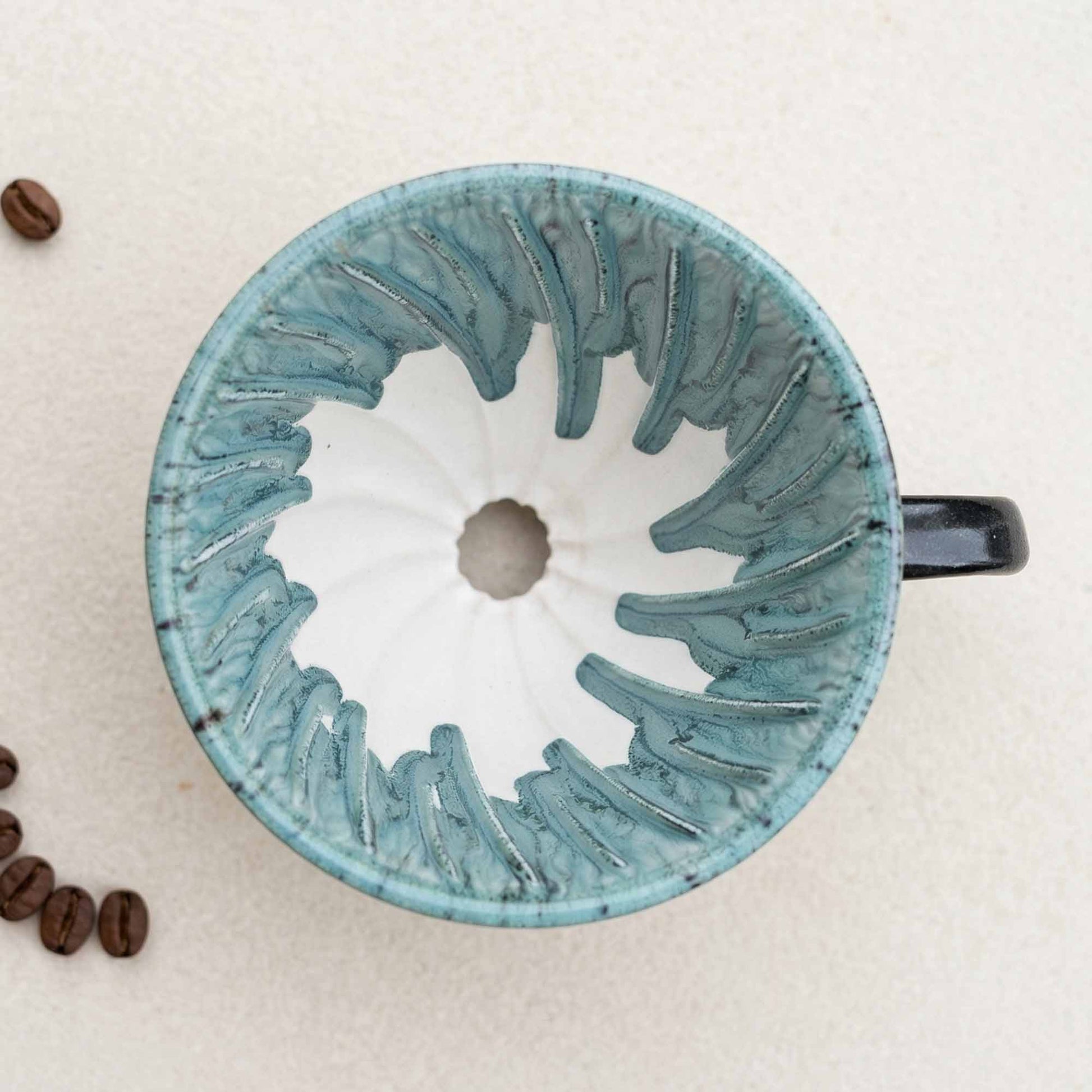 Ceramic coffee filter with textured design on a beige background with coffee beans.