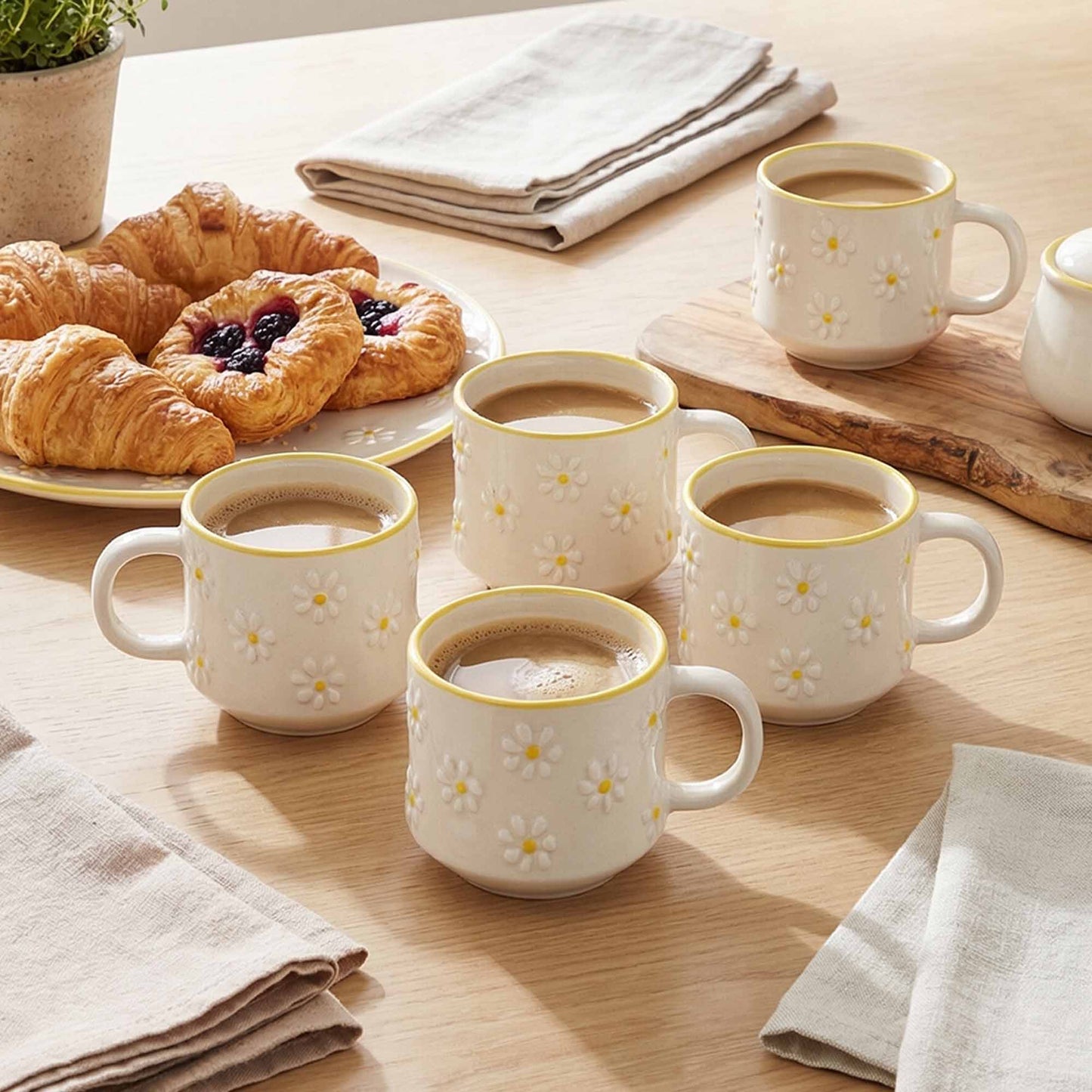 Set of four white mugs with yellow floral patterns filled with coffee on a wooden table with pastries.
