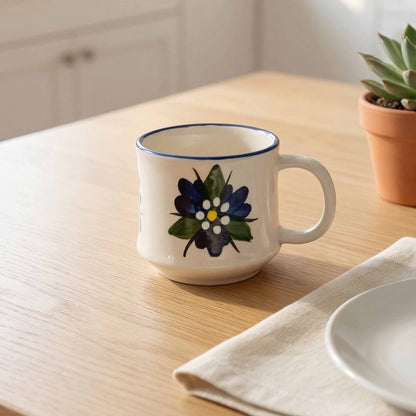 White mug with floral design on a wooden table with a plant and plate in the background