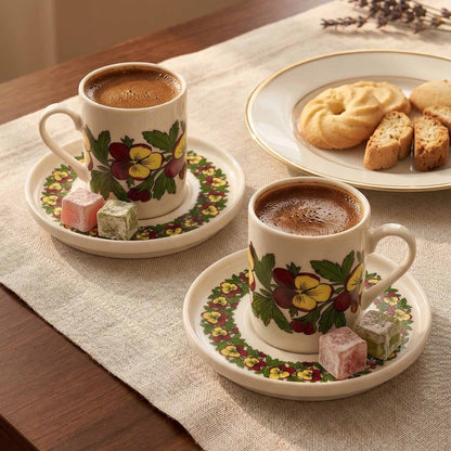 Two cups of coffee with floral designs on saucers, accompanied by cookies and pastries on a table.