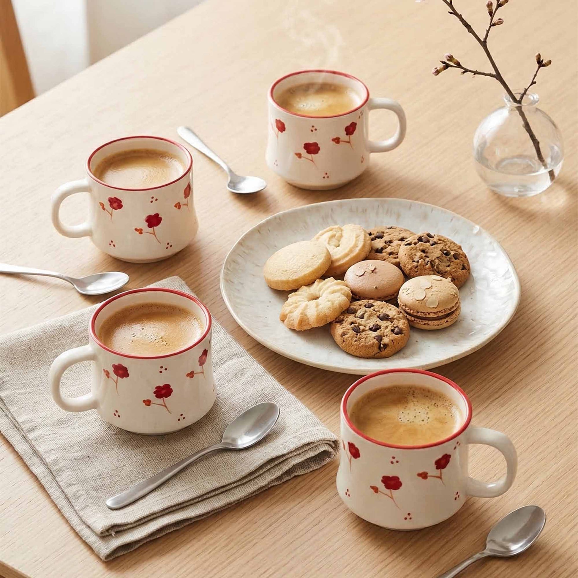 Four coffee mugs with floral design on a table with cookies and spoons.