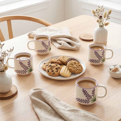 Table setting with coffee mugs, cookies, and a plate of pastries on a wooden table.