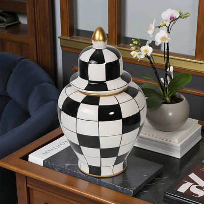 Black and white checkered jar with gold accents on a table next to a potted plant.