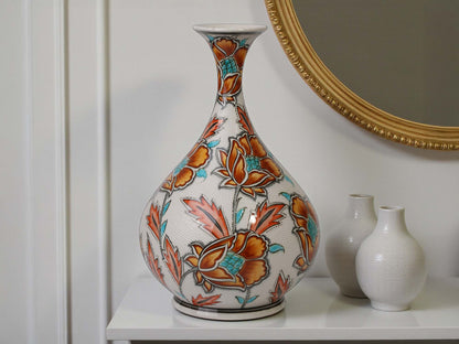 Decorative ceramic vase with floral patterns on a white surface, with a mirror in the background.