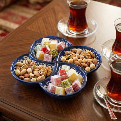 Nuts and pastries in a divided dish with glasses of tea on a wooden table.