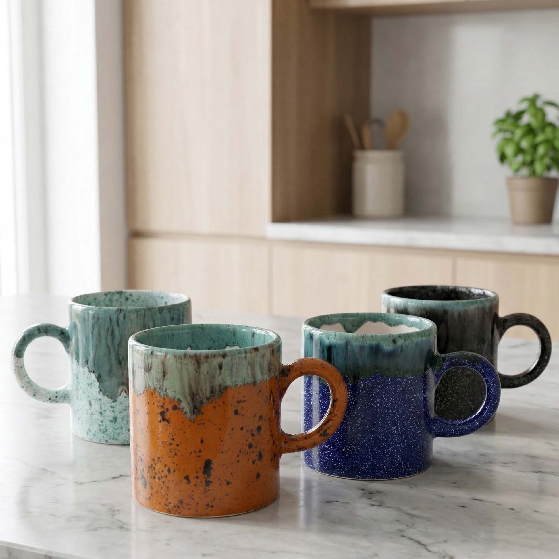 Set of four ceramic mugs with gradient colors on a marble countertop.