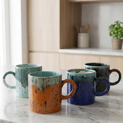 Set of four ceramic mugs with gradient colors on a marble countertop.