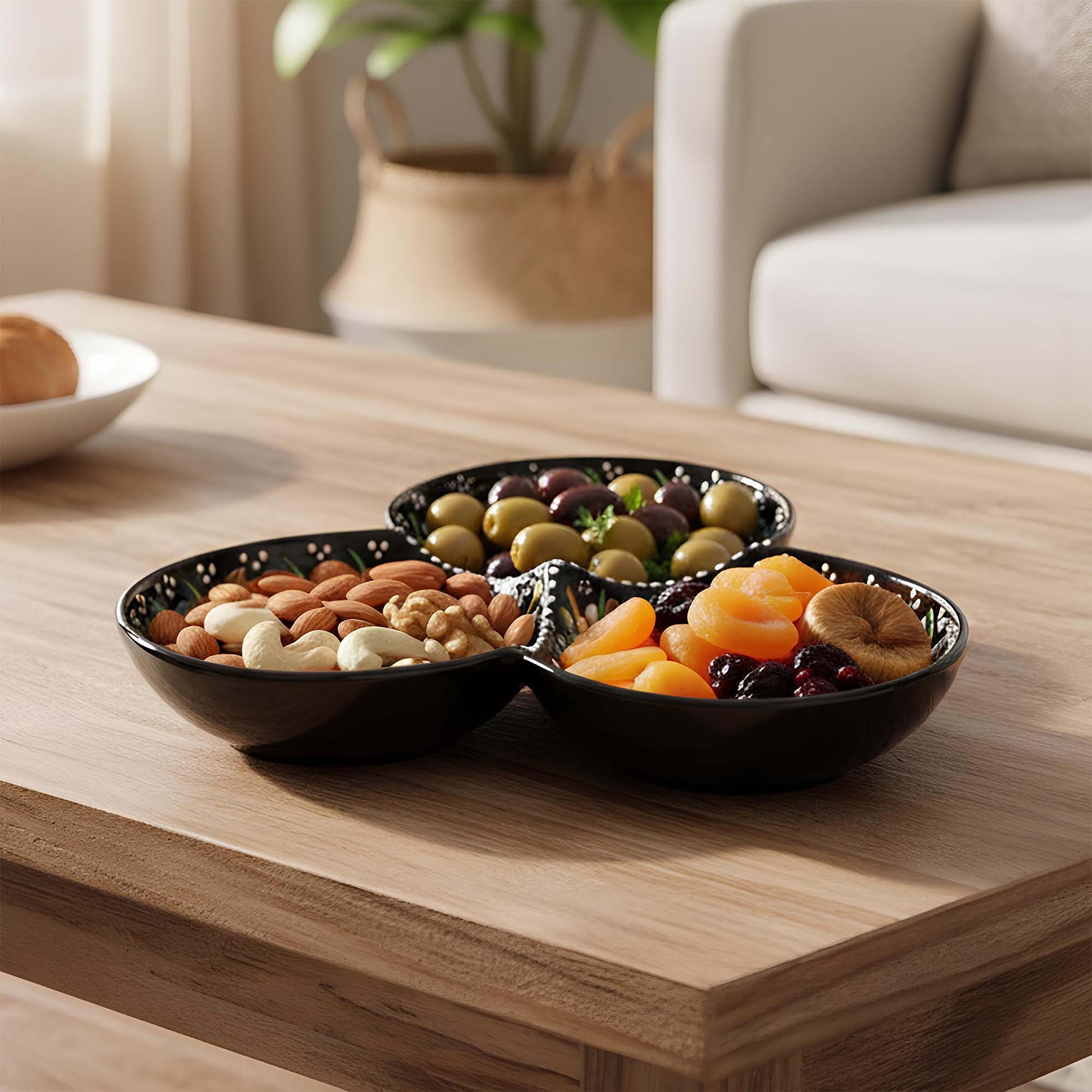 Three-section black bowl with assorted nuts and dried fruits on a wooden table.