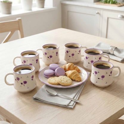 Set of six floral coffee mugs on a table with pastries and cookies.