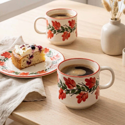 Two floral-patterned mugs with coffee and a slice of cake on a wooden table.