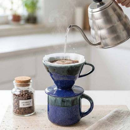 Person pouring water from a kettle into a blue ceramic coffee filter on a wooden surface.