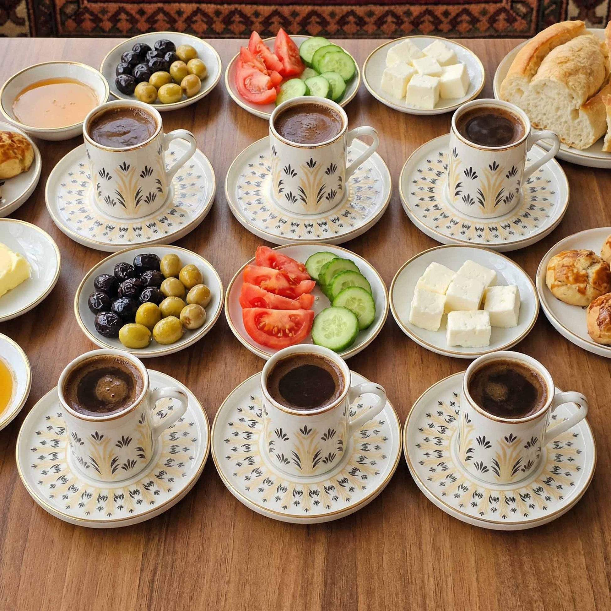 Café with cups of coffee, plates of food including olives, tomatoes, and bread on a wooden table.