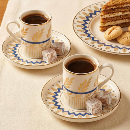 Two cups of coffee with pastries on decorative plates on a beige tablecloth.