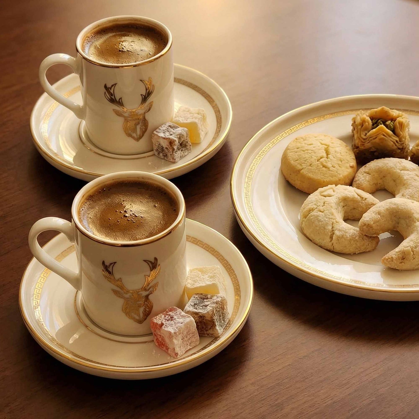 Two cups of coffee with saucers and a plate of cookies and pastries on a wooden table.