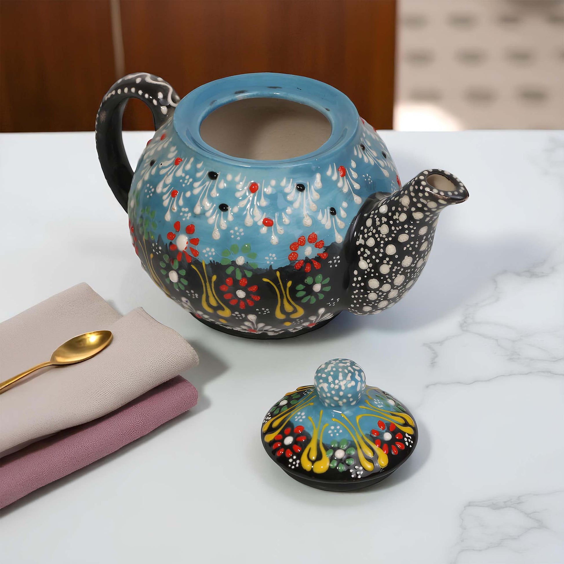Decorative ceramic teapot with floral patterns on a marble surface.