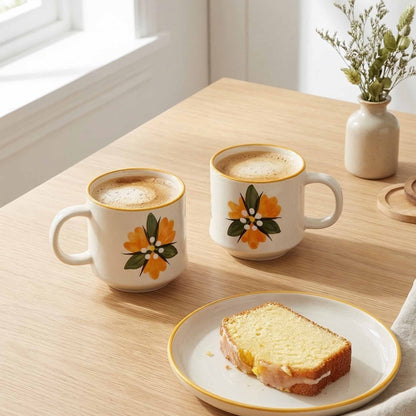 Two floral-patterned mugs with coffee and a slice of cake on a wooden table.