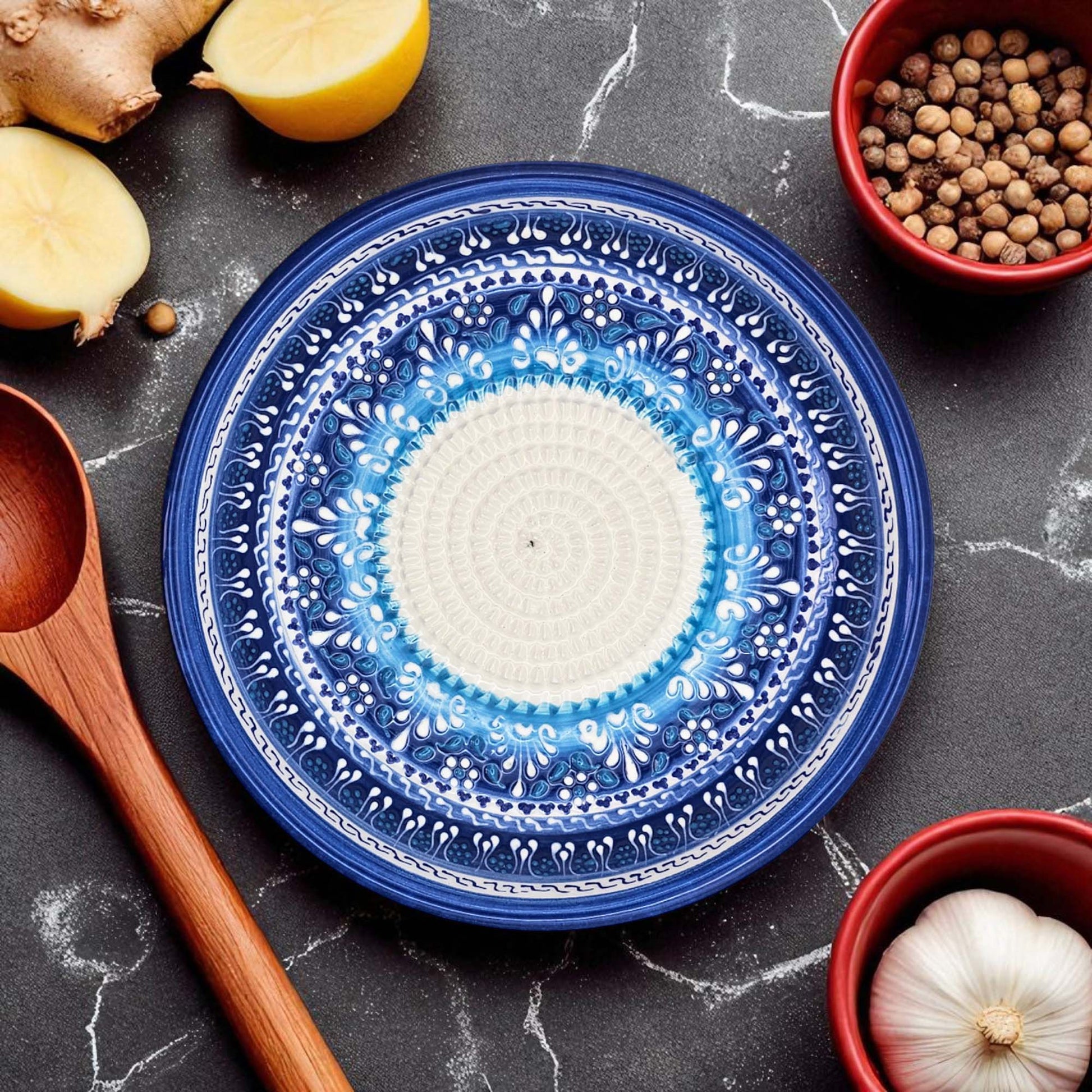Blue decorative garlic grater bowl with intricate patterns on a dark surface with kitchen items.