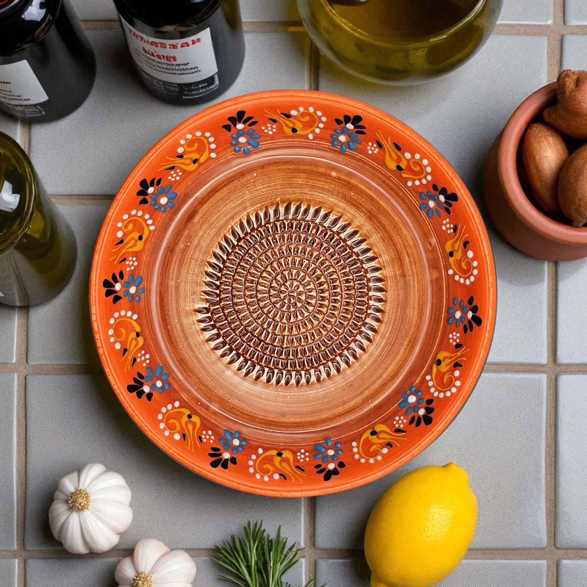 Decorative ceramic garlic grater bowl with floral patterns on a tiled surface with lemons and bottles.