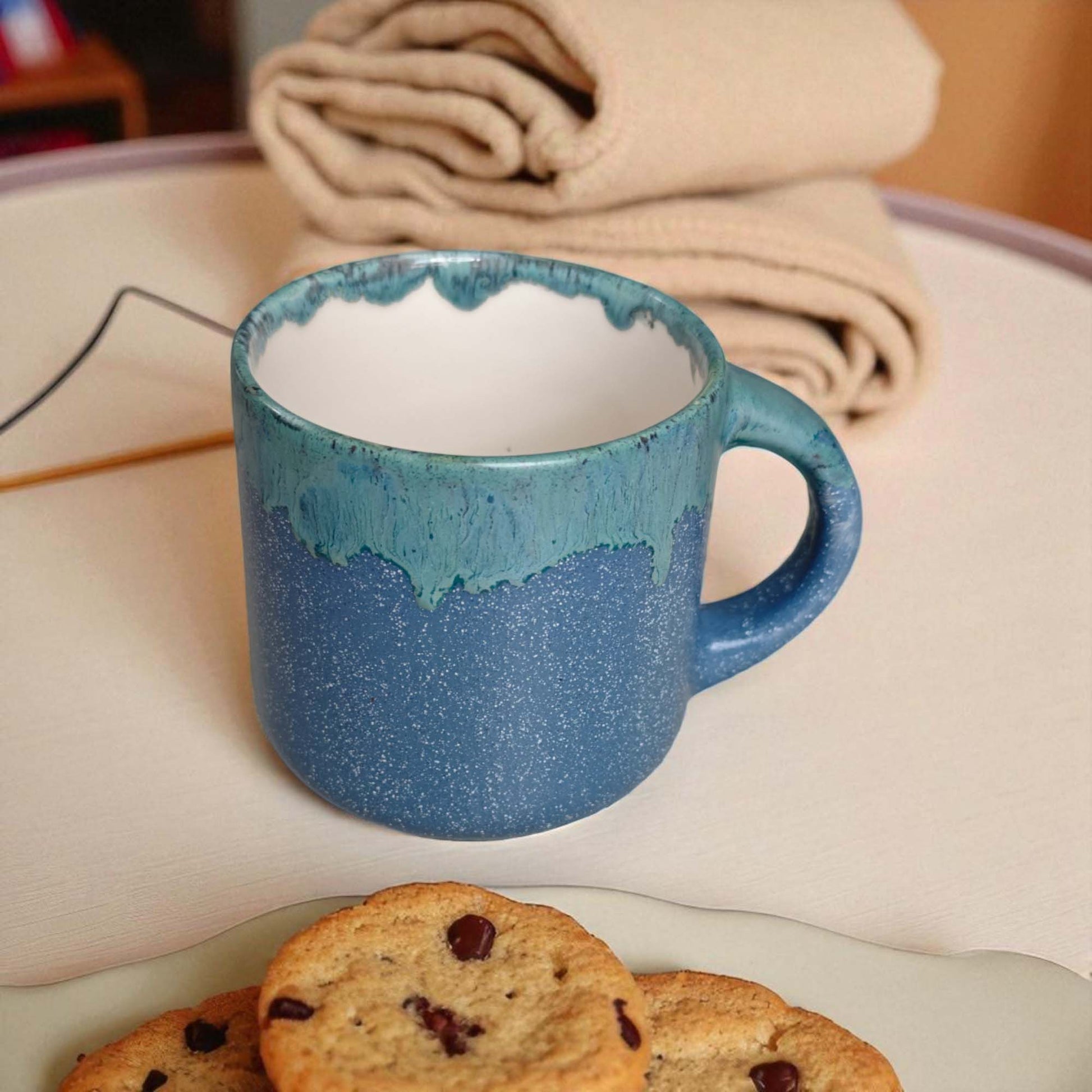Blue ceramic mug on a surface with cookies and folded fabric in the background