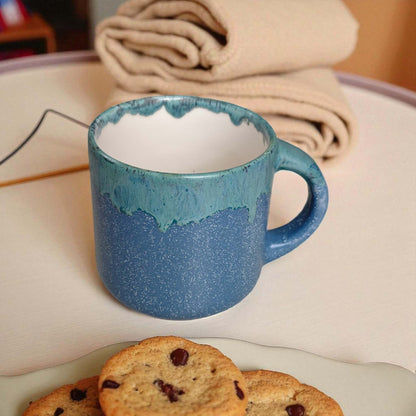 Blue ceramic mug on a surface with cookies and folded fabric in the background